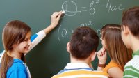 Middle school students discuss math problems written on a blackboard.