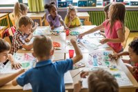 A group of elementary students create art at a large table together in a classroom