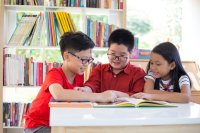 Three elementary students reading together in a library 