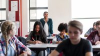 A student standing up confidently in the back of a classroom, answering a question