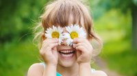 Elementary-aged girl playfully holds daisies over her eyes