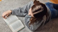 Teenage girl reading book on floor at home. 