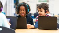 Two elementary students working on laptops in class