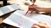 Teacher grading a writing assignment with a red pencil