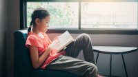 Middle-school aged girl reads a book while sitting in front of a window