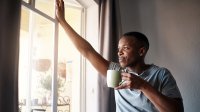Man in the morning, looking out window holding coffee