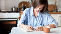 Woman writing in a notebook while sitting at her kitchen table