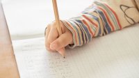 Close up of child's hand as they do math work in notebook. 