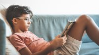 Middle school aged boy reading book on couch at home