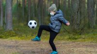 Boy kicking a soccer ball outside while wearing a mask