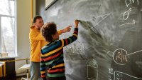 Teacher with student doing math on chalkboard