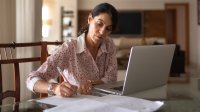 Woman working on her laptop and taking notes at home