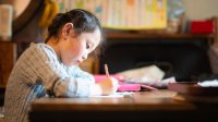 Elementary-aged girl writes on paper at home