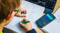 Teenage boy doing math homework with calculator and computer