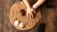 Child's hands pushing objects from nature into clay