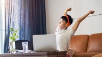 Teenaged boy takes a break to stretch while working at his laptop at home