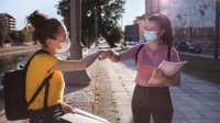 Two teenage girls greet each other with a fist bump on an urban sidewalk