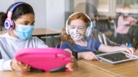 Two elementary students work together on their tablets while wearing masks in socially-distanced classroom