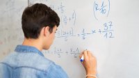 High school student works on math problems at whiteboard