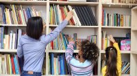 Teacher helps student reach library book off a high shelf