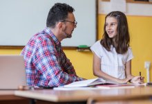 A teacher and elementary school student speak at the teacher's desk