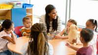 Preschool teacher sits a table with a small group of her students