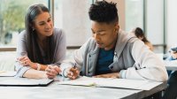 High school teacher talks to student at his desk