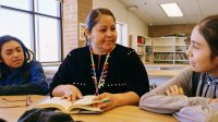 A middle school teacher talks with two students in a library