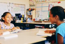 Two elementary school students reading and discussing books in class