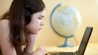 Pre-teen girl looks at laptop screen with a globe in background. 