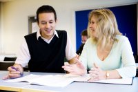 Two adults sitting and talking with papers in a classroom