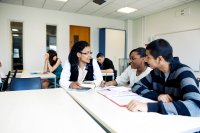 A teacher meeting with two students in a classroom, giving them feedback on their recent work