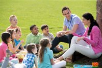 A teacher and her TA conducting class outside in a grassy field under a tree