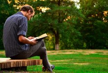 Man reading a book while sitting on a park bench