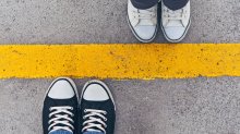 A photo of two pairs of feet stepping up to a yellow line in the road