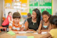 A teacher helping elementary students with a reading and writing assignment in class