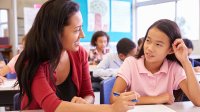 Teacher helps elementary student with work in classroom