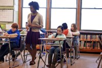 Middle school teacher walking among students writing at their desks