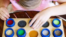 Child with poor vision is touching the wooden tactile rolls of different texture and colour as a part of educational therapy.