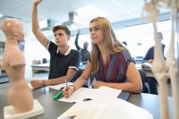 Students in a biology class, surrounded by human anatomical models and paper handouts