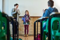 An elementary student presents her findings for a PBL project to her class. Her teacher stands next to her, applauding.