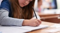 A older elementary girl writes in notebook at school desk. 