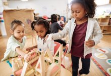 A group of young children building a house out of blocks together in a classroom