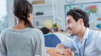 Teacher kneeling down to talk with a student at her desk