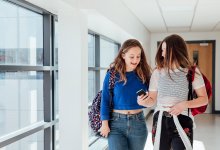 Middle school students walk down school hallway with phone