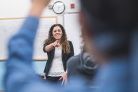 A teacher smiling and pointing to a student in the foreground who is raising his hand