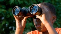 Boy looking through binoculars outside.