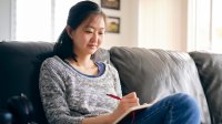 Adult woman writing in journal at home on couch