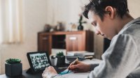 Teenage boy at home attending online class on iPad. 