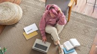 Teenage girl sitting on floor at home doing homework with laptop and books